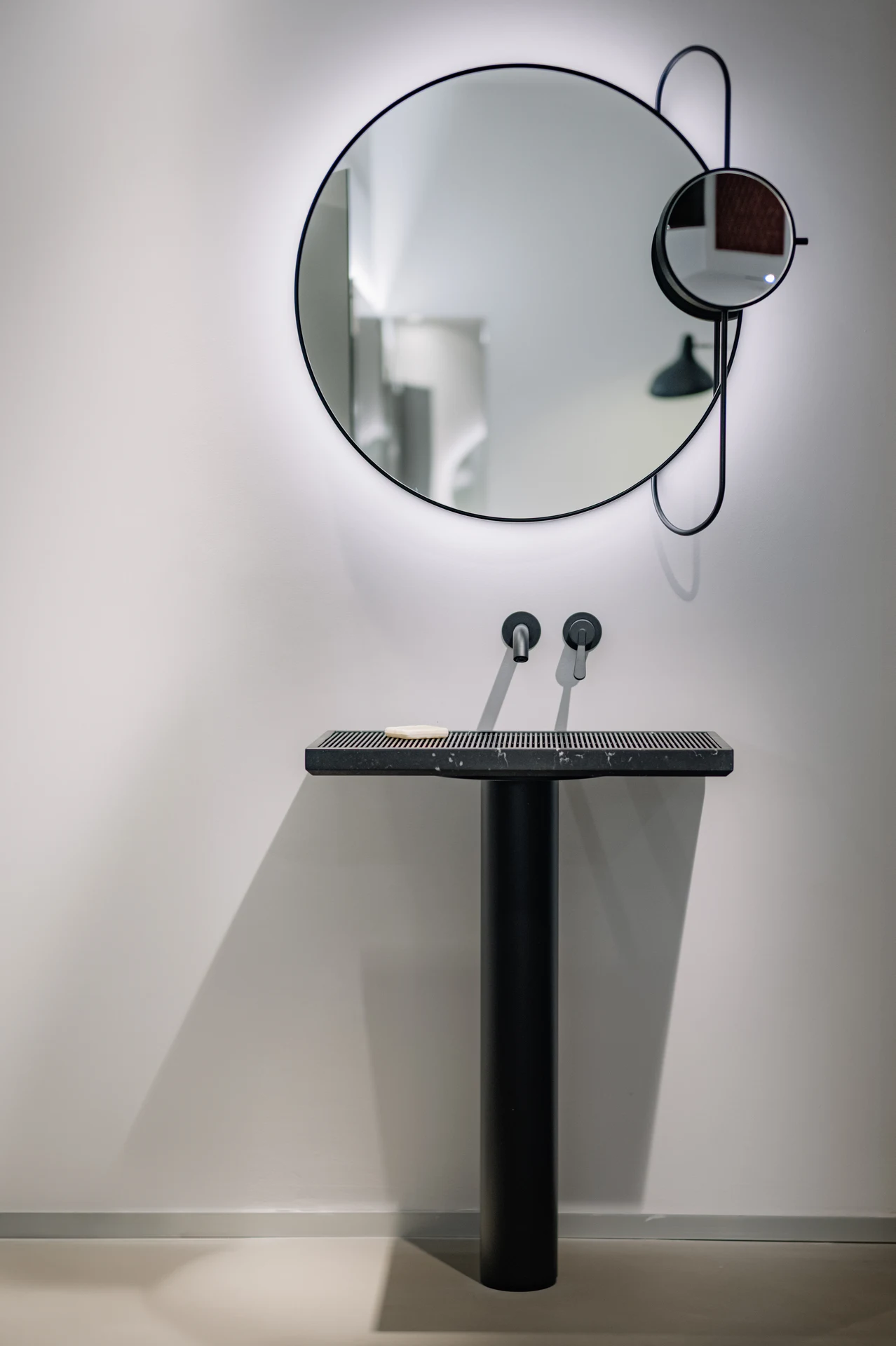 Miroir Agape Revolving Moon au-dessus d’un lavabo sculptural noir, dans le showroom de Milan.